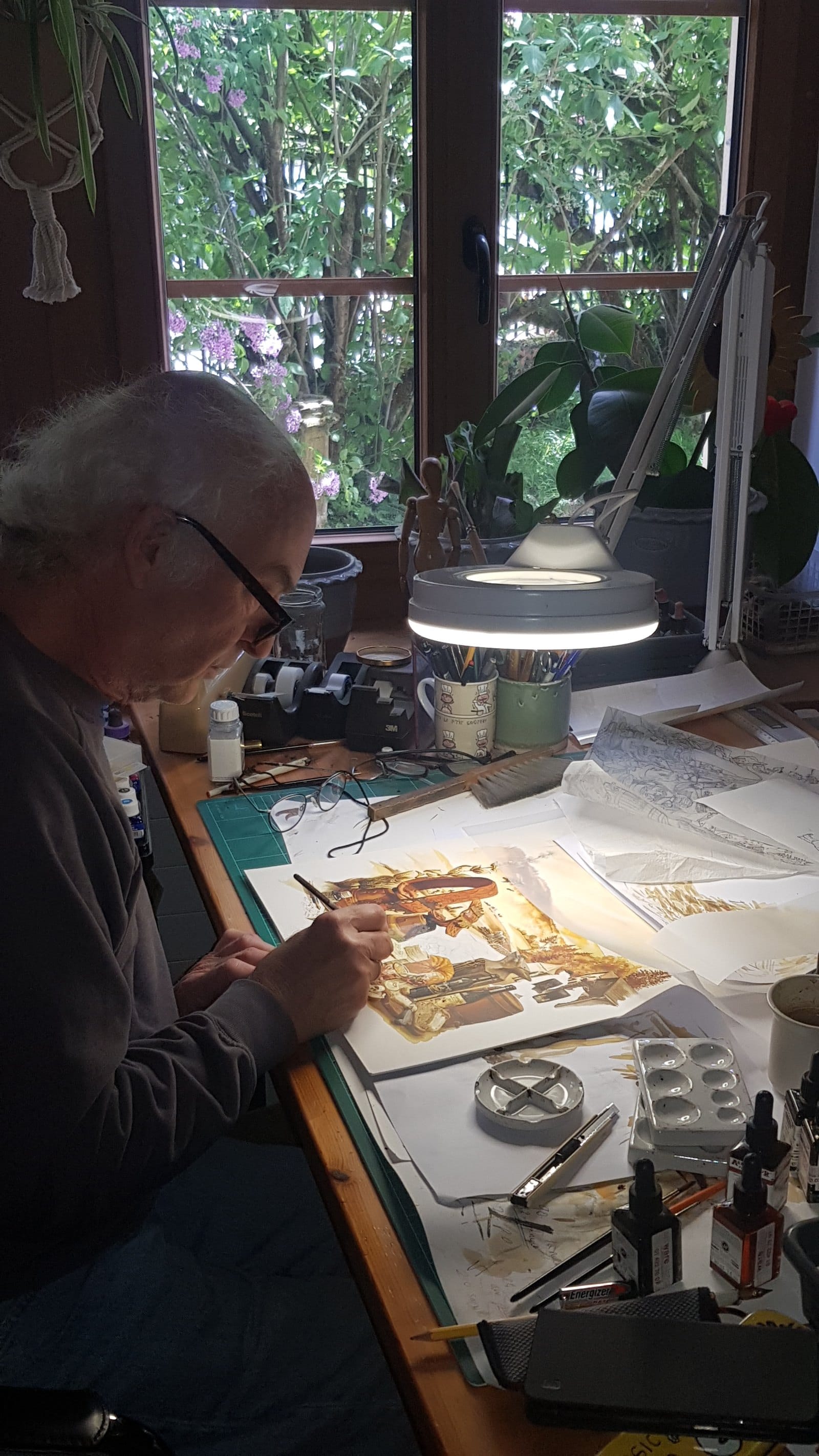À sa table, l'aquarelle en cours et les crayonnés à côté.